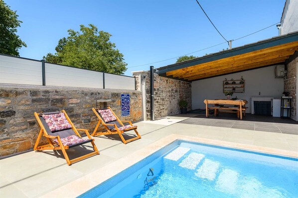 Une piscine avec des chaises longues, un mur en pierre et un patio couvert comprenant une table et des chaises.