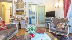 Un salon avec deux fauteuils, une table basse sur laquelle se trouvent un livre et un vase de fleurs, un téléviseur et un miroir décoratif.