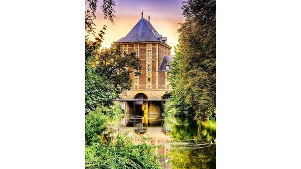 Un edificio histórico con una torre destacada, un puente y un reflejo en el agua.