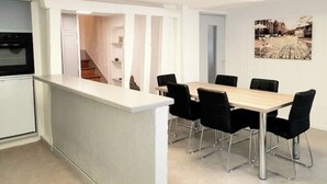 Una cocina moderna con una isla integrada, un comedor con mesa de madera y sillas negras, y una escalera que sube a un nivel superior.