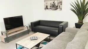 Una sala de estar moderna con un sofá de cuero negro, una mesa de centro de madera y un televisor de pantalla plana sobre un mueble de madera.