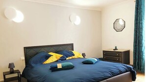Un dormitorio con una cama grande, una mesita de noche, un aparador y una lámpara fijada a la pared.