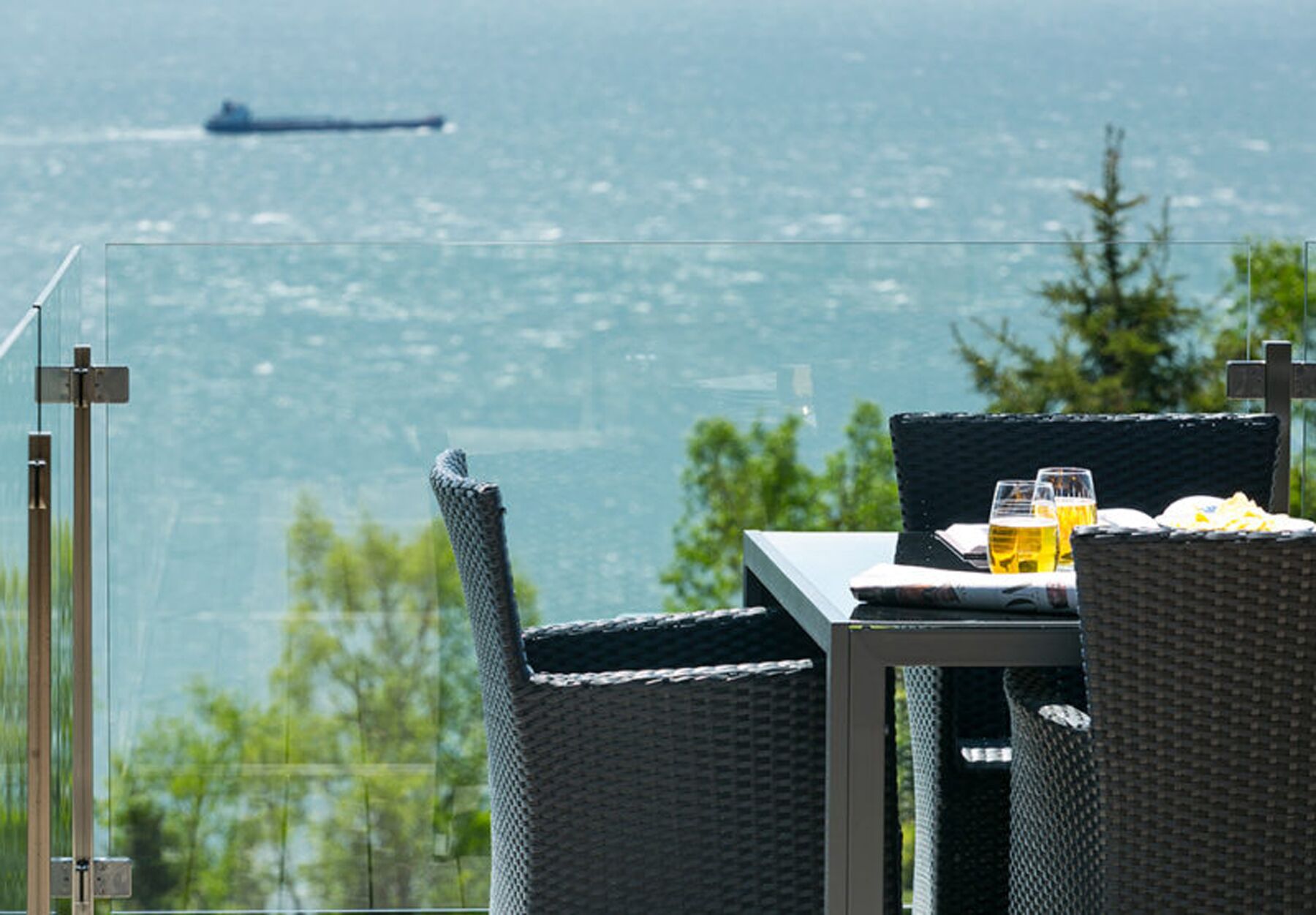 A dining area with a table and chairs, overlooking a body of water with a ship in the distance.