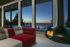 A modern living room with a red sofa, large windows, and a wood-burning stove. - Breathtaking views, privacy, and fresh air. (La Malbaie)
