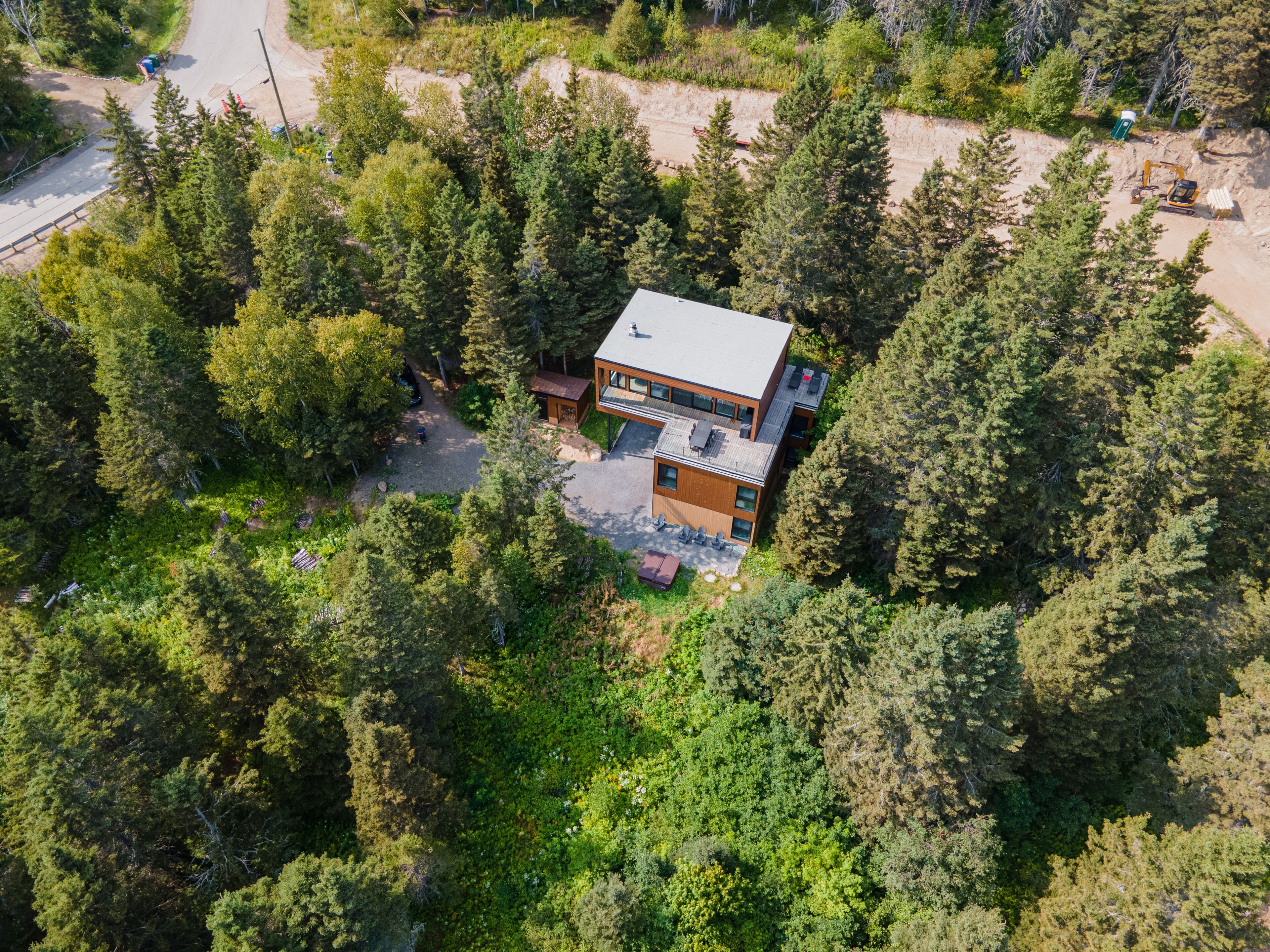 An aerial view of a modern two-story house surrounded by dense forest.