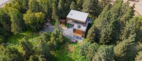 An aerial view of a modern two-story house surrounded by dense forest.