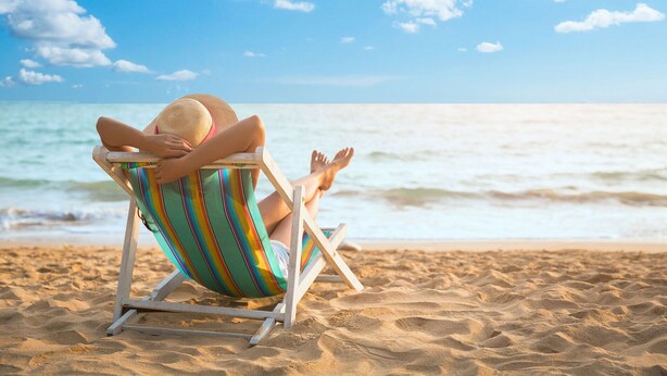 A person sitting in a beach chair on a sandy beach with the ocean in the background. - Recently Renovated Spacious 6 Bedroom Condo, Just Steps From The Ocean (Ocean Isle Beach)
