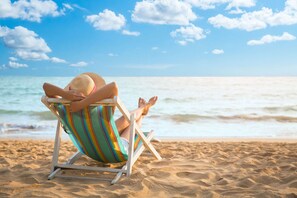 A person sitting in a beach chair on a sandy beach with the ocean in the background. - Recently Renovated Spacious 6 Bedroom Condo, Just Steps From The Ocean (Ocean Isle Beach)