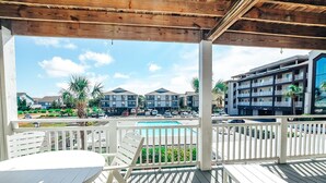 A covered outdoor area with a pool, white furniture, and a view of a multi-story building with balconies. - Recently Renovated Spacious 6 Bedroom Condo, Just Steps From The Ocean (Ocean Isle Beach)