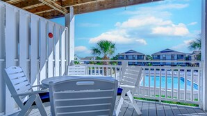 A covered outdoor area with white chairs and a pool. - Recently Renovated Spacious 6 Bedroom Condo, Just Steps From The Ocean (Ocean Isle Beach)