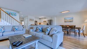 A modern living room with a grey sofa set, a coffee table, and a dining area with wooden chairs and a table. - Recently Renovated Spacious 6 Bedroom Condo, Just Steps From The Ocean (Ocean Isle Beach)