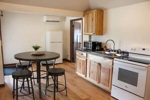A compact kitchen with a round dining table, stools, a microwave, a sink, and wooden cabinets. - Horse Creek Resort - Cabin 1 (Rapid City)