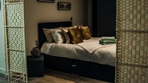 A bedroom with a bed, pillows, a bedside table, and a wardrobe. - Bv Cosy Basement Apartment At Conditioning House (Bradford)