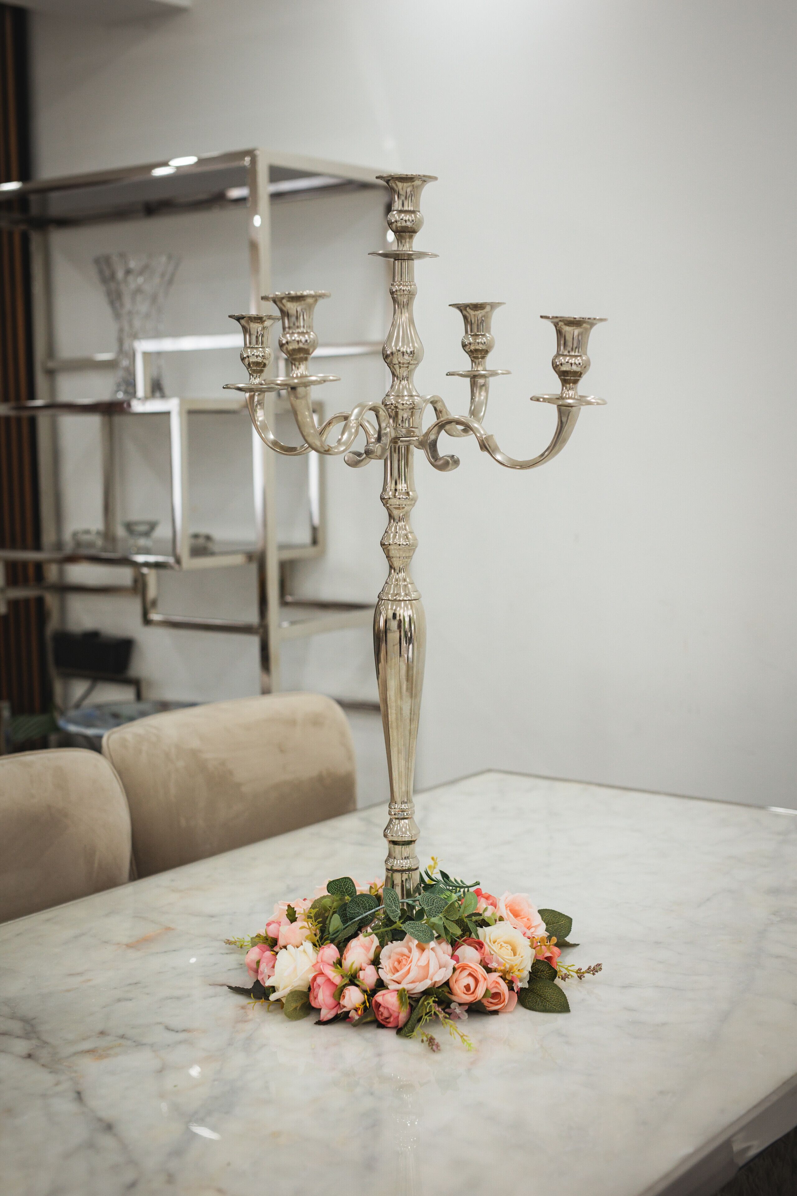 A candelabra with multiple candle holders on a marble table, surrounded by a floral arrangement.