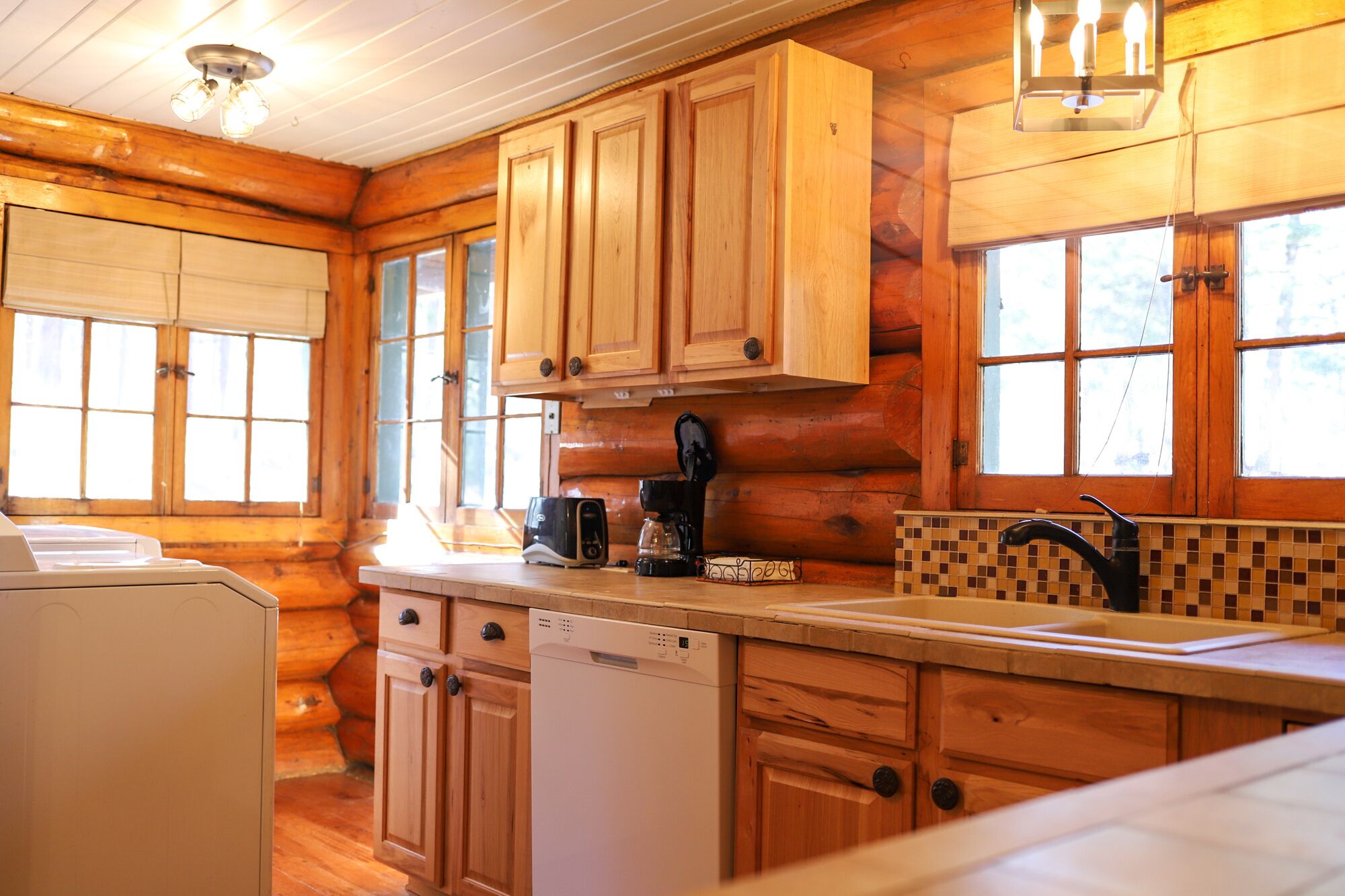 A log cabin kitchen with wooden cabinets, a coffee maker, a dishwasher, and a window with a view.
