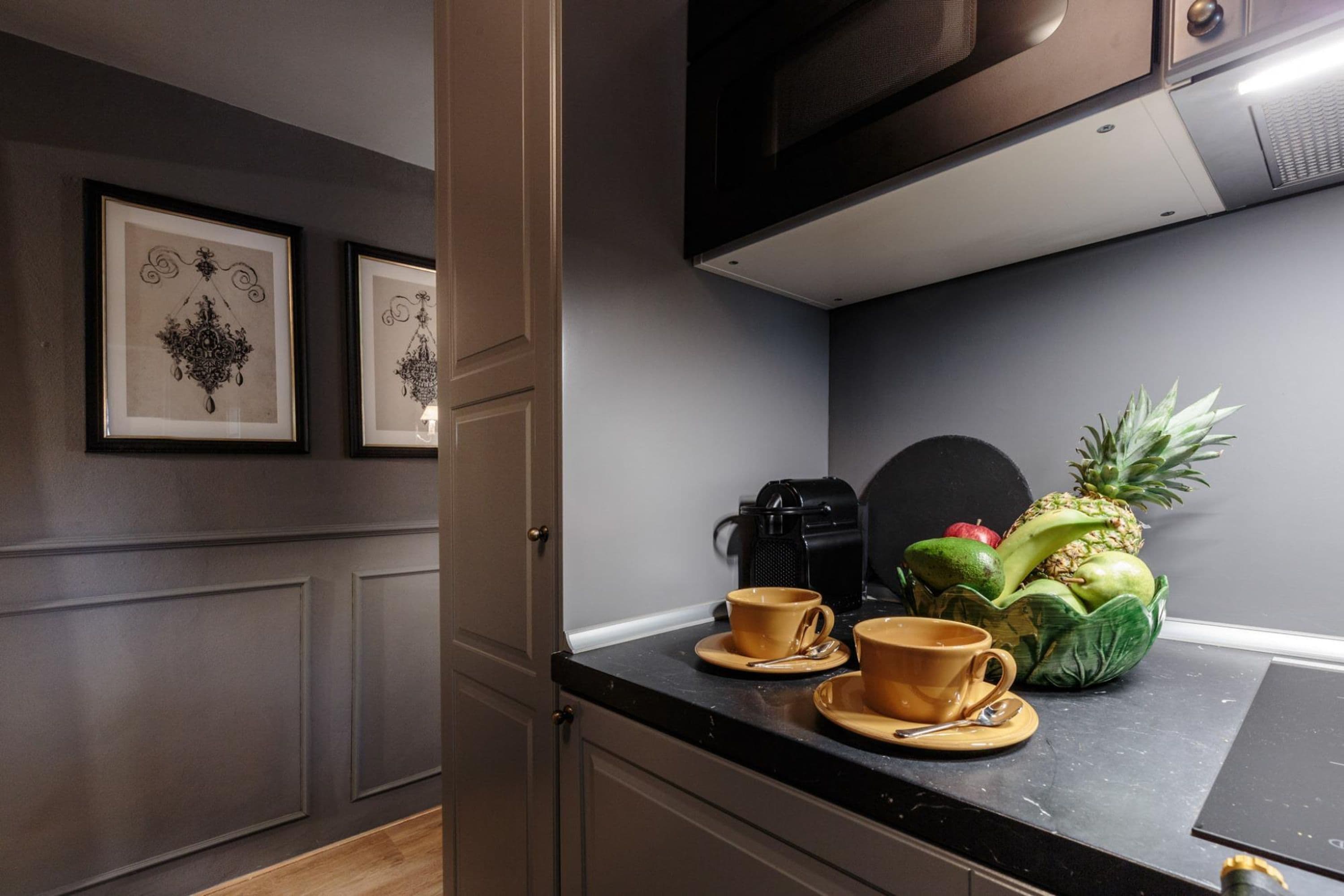 A kitchen with a black countertop, a coffee maker, two cups, and a pineapple.