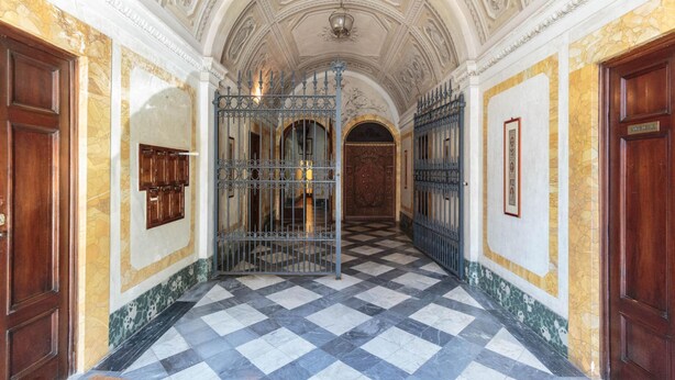A hallway with a checkered floor, ornate ceiling, and metal gates. - Casa Palatial in Lucca (Lucca)