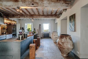 A spacious kitchen with a central island, wooden beams on the ceiling, and large vases on the floor.