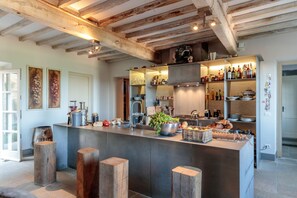 A modern kitchen with a central island, wooden stools, and a variety of kitchen appliances and utensils.