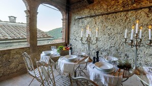 A dining area with a rustic stone wall, a table set for four, and a view of a tiled roof through an archway. - Palazzo Giusti in Pescaglia (Pescaglia)