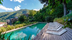 A wooden deck with a swimming pool, surrounded by lush greenery and overlooking a village with traditional buildings. - Palazzo Giusti in Pescaglia (Pescaglia)