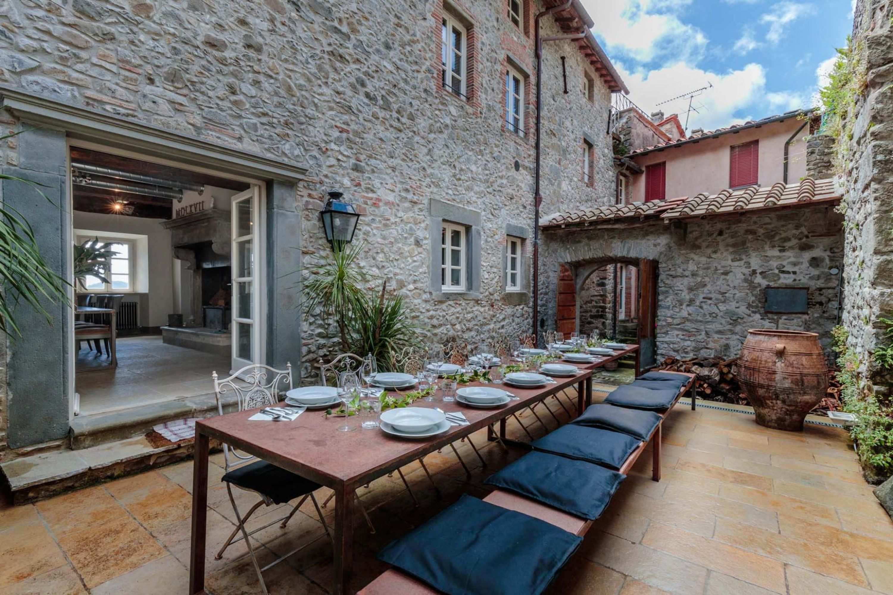 A stone building with a long dining table set for a meal, benches, and a large pot.
