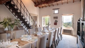 A dining area with a long table set for a meal, a staircase, and a view of the outdoors. - Palazzo Giusti in Pescaglia (Pescaglia)