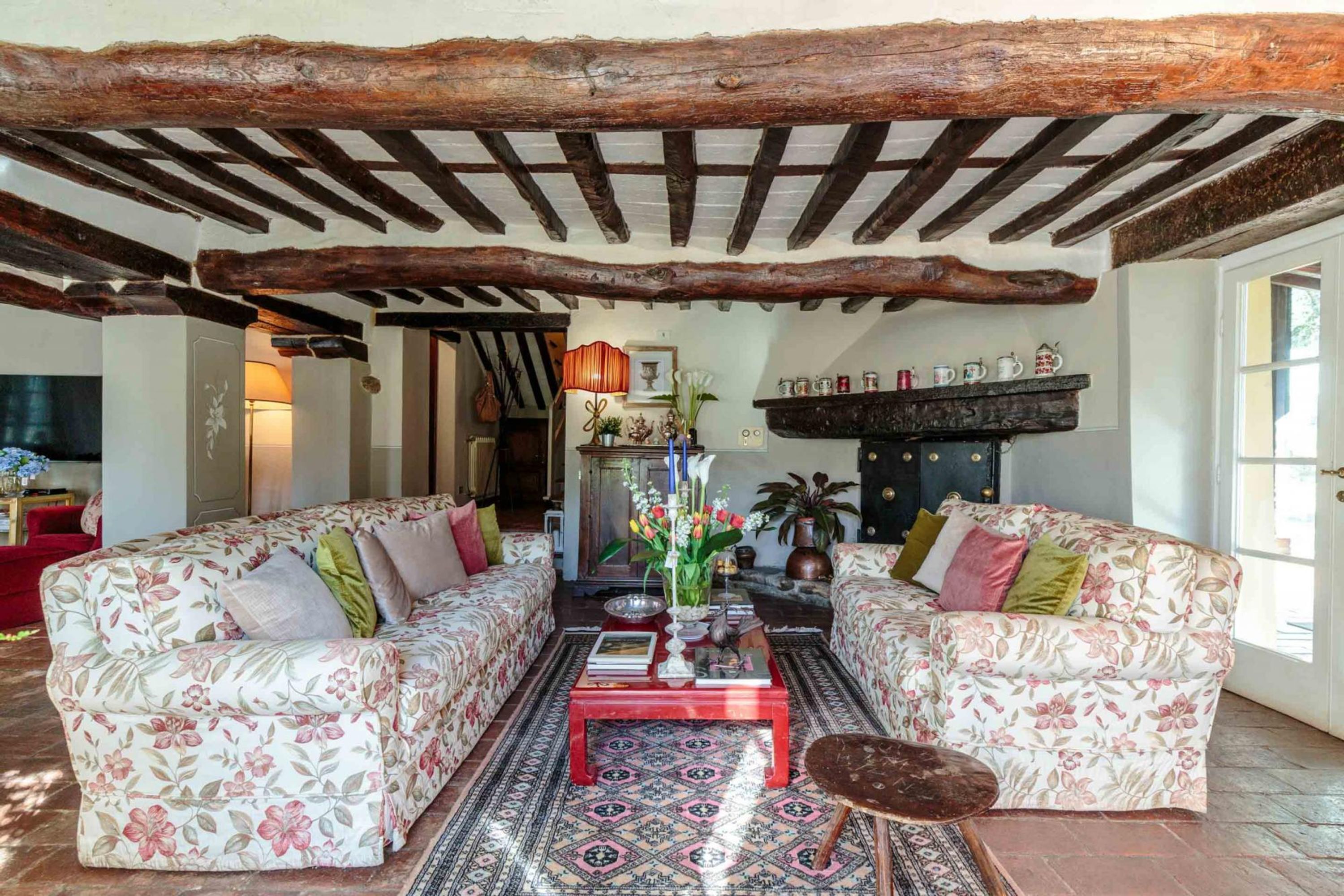 Una sala de estar acogedora con dos sofás de estampado floral, una mesa de centro roja y un tapete con motivos.