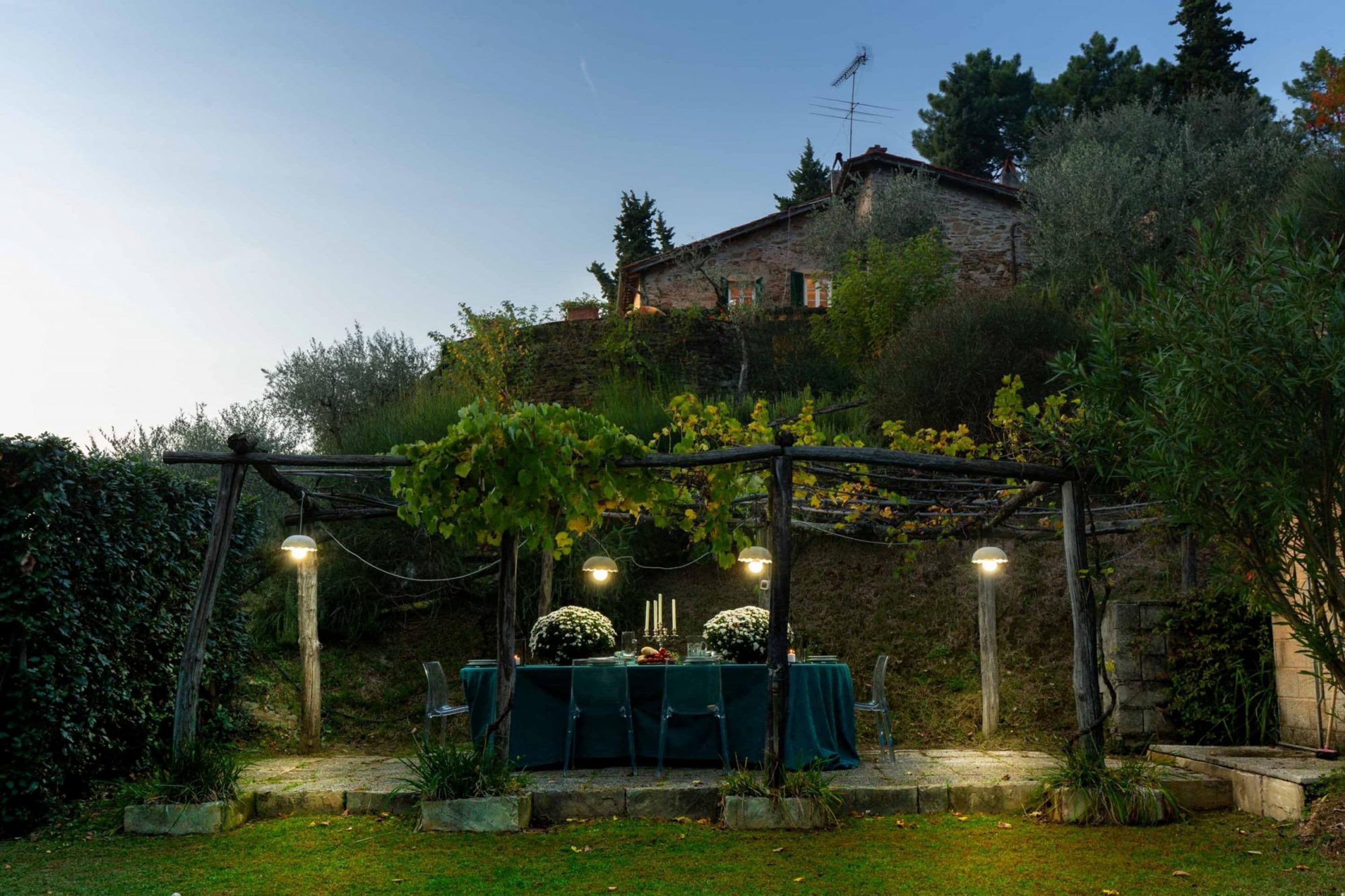 An outdoor dining area with a table set for four, surrounded by greenery and a stone wall.