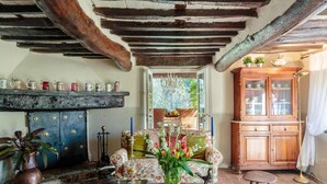 A rustic room with exposed wooden beams, a floral sofa, a wooden cabinet with glass doors, and a vase with flowers on a table. - Casa Nel Bosco in Santa Maria del Giudice (Lucca)