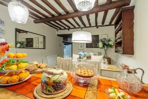 A dining area with a wooden table set for a meal, featuring a variety of fruits, pastries, and a pie on a wooden board. - Casa Nel Bosco in Santa Maria del Giudice (Lucca)