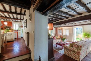 A rustic interior with exposed wooden beams, a kitchen with a tiled floor, and a living area with a sofa and a coffee table.