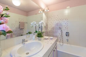 A bathroom with a white sink, a bathtub, and a shower. There are decorative flowers and a towel rack.