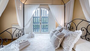 A bedroom with a canopy bed, white linens, and a view of a wooden gate through a glass door. - Villa sul Fiume in Monte San Quirico (Lucca)