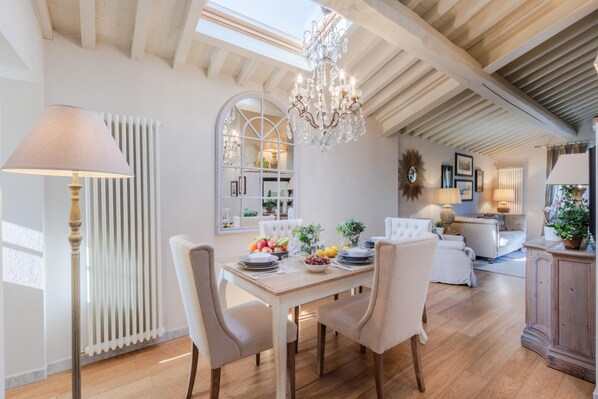 Un coin repas avec une table en bois dressée pour quatre personnes, entourée de chaises, d’un lustre et d’un radiateur.