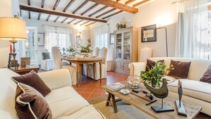 A cozy living room with a wooden ceiling, a dining area with a table set for four, and a comfortable sofa. - Villa Alberta in Lucca (Lucca)