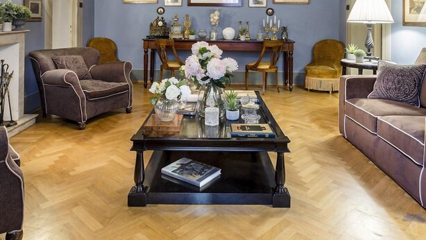 A room with a chandelier, framed pictures on the wall, and a coffee table with flowers. - Casa Barbra in Lucca (Lucca)