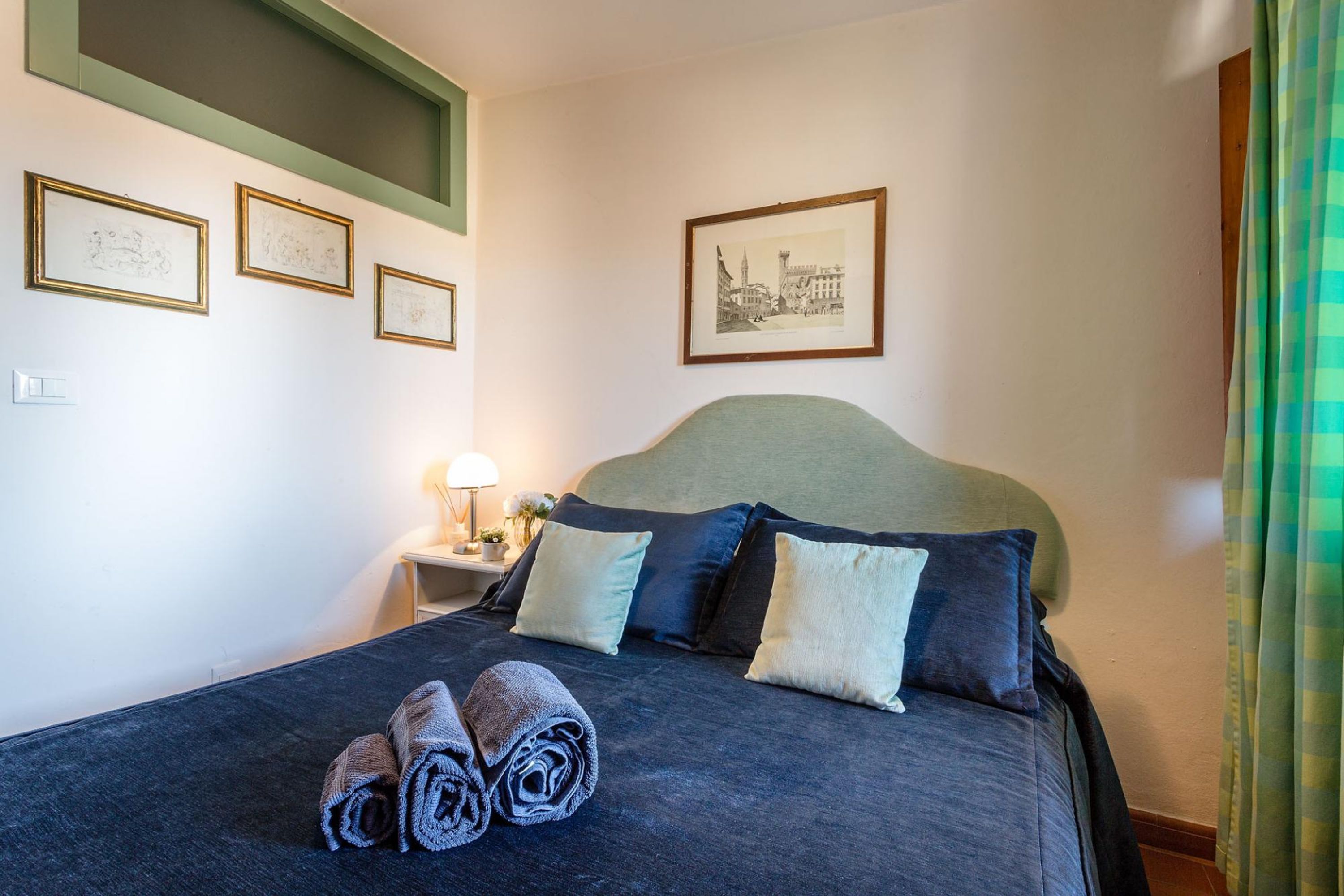 En pænt redt seng med sammenrullet håndklæder, en sengegavl og et natbord med en lampe.