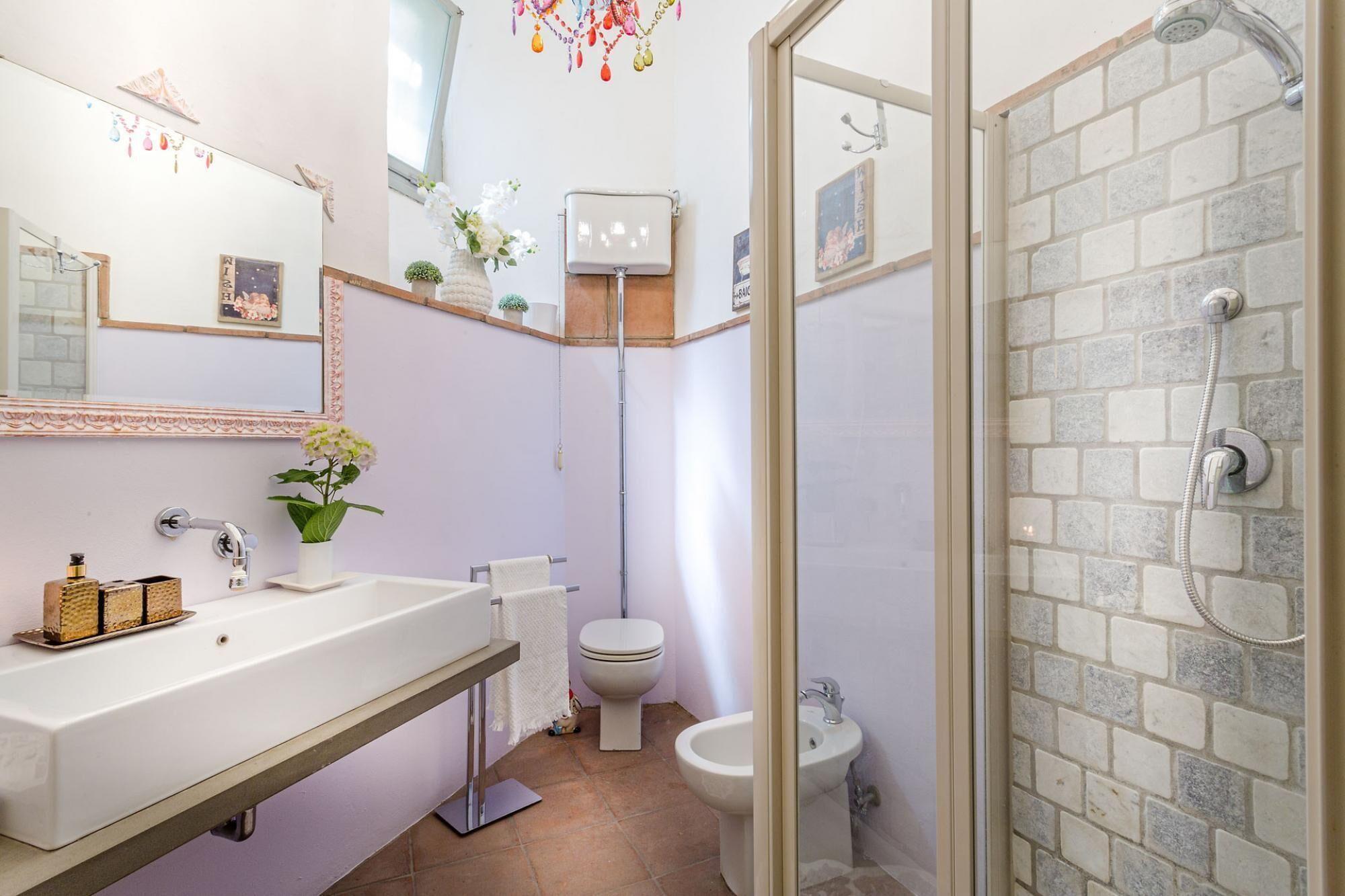 A bathroom with a white sink, a toilet, a bidet, and a shower area with a tiled wall.