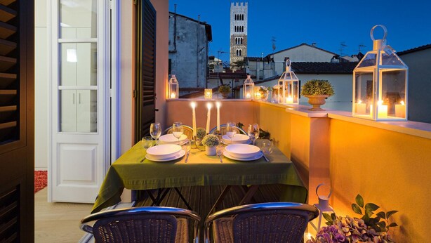 An outdoor dining area with a table set for four, surrounded by wicker chairs, under a night sky with a tower in the background. - Casa Cachi 2 in Lucca (Lucca)