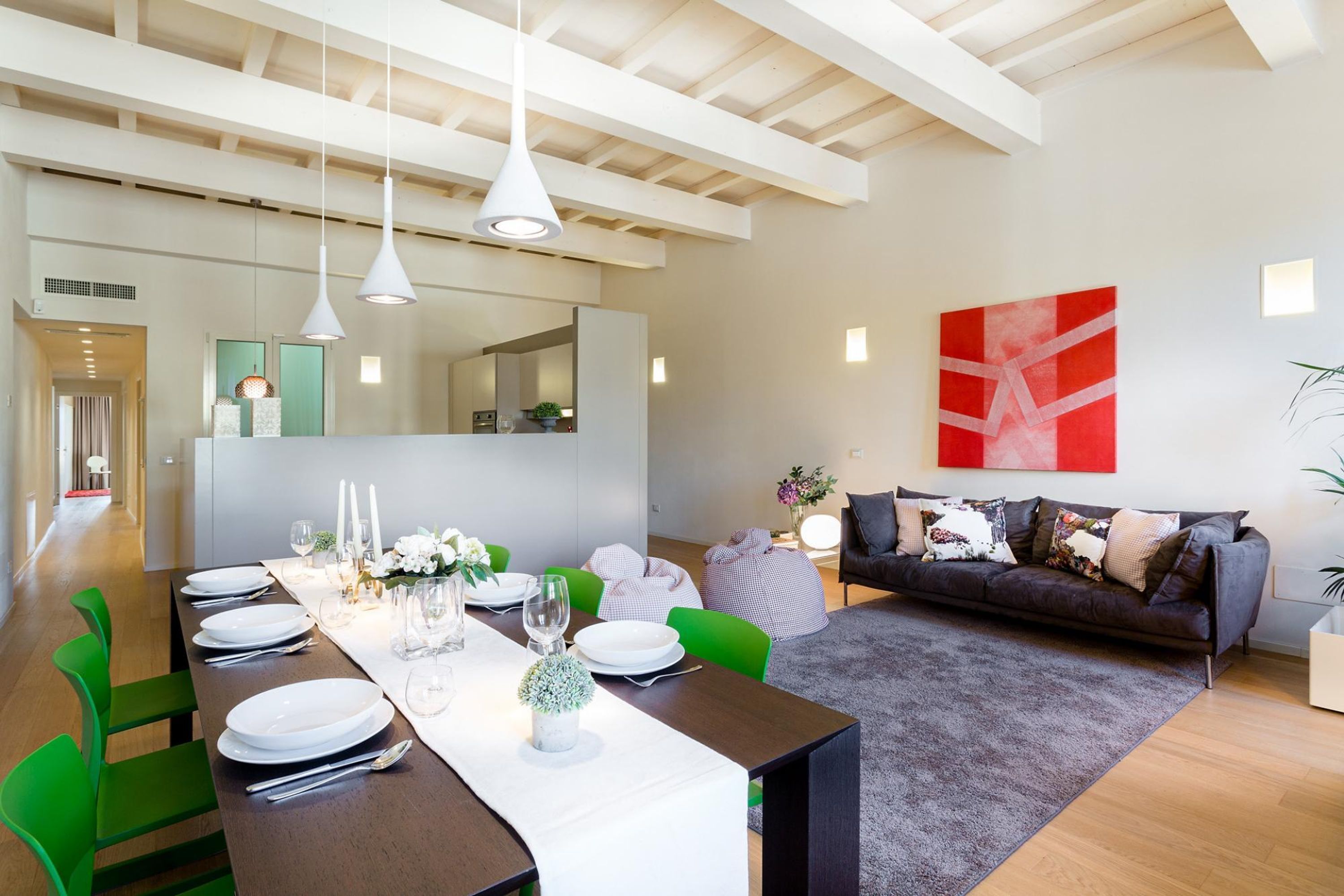 A modern dining area with a long table set for six, green chairs, and pendant lighting.
