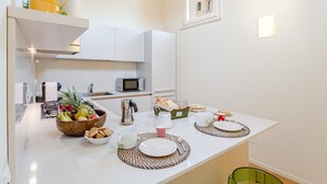 A modern kitchen with white cabinets, a microwave, and a breakfast setup including fruits, bread, and cups.