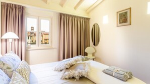 A hotel room with a bed, curtains, a lamp, a framed picture, and a view of buildings outside the window.