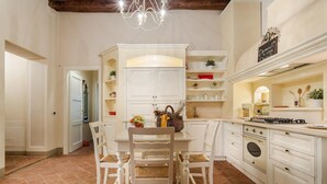 A kitchen with white cabinetry, a dining table with four chairs, a chandelier, and a stove. - Casa Daniela in Lucca (Lucca)