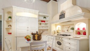 A kitchen with white cabinetry, a gas stove, and a dining area with a table and chairs. - Casa Daniela in Lucca (Lucca)