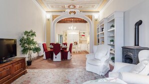 A living room with a TV, a fireplace, and a dining area with red chairs. - Casa Daniela in Lucca (Lucca)