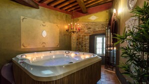 A hot tub in a rustic room with wooden beams, stone walls, and a chandelier. - La Dimora dei Conti in Capannori (Capannori)