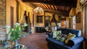 A cozy living room with a dark blue sofa, a vase of flowers, and a rustic kitchen in the background. - La Dimora dei Conti in Capannori (Capannori)