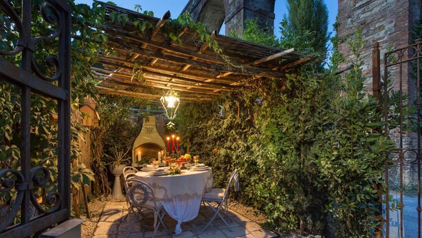 An outdoor dining area with a pergola, rustic brick walls, and a stone archway. - La Dimora dei Conti in Capannori (Capannori)