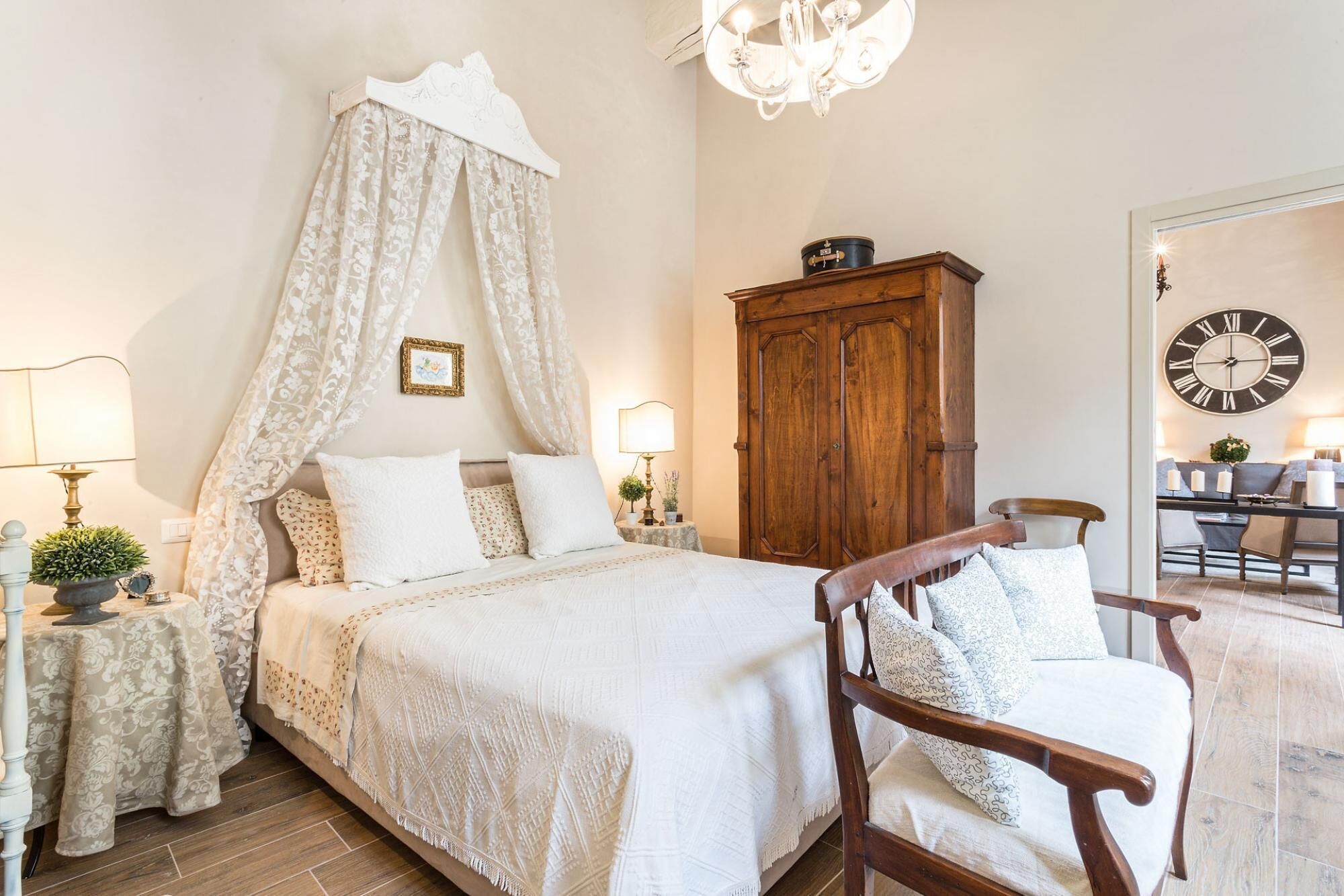 A bedroom with a four-poster bed, a wooden wardrobe, a wooden chair, and a large wall clock.